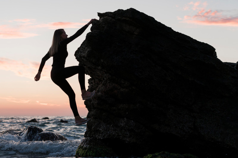 Woman Climbing Jugged Rock Next To Ocean