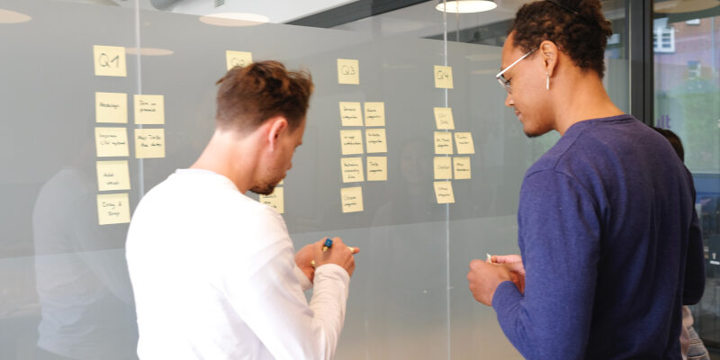 Two Men Mapping Out Strategy and Tactics On White Board With Post It Notes