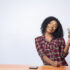 Confident black lady sitting and holding a wad of cash with cellphone on desk