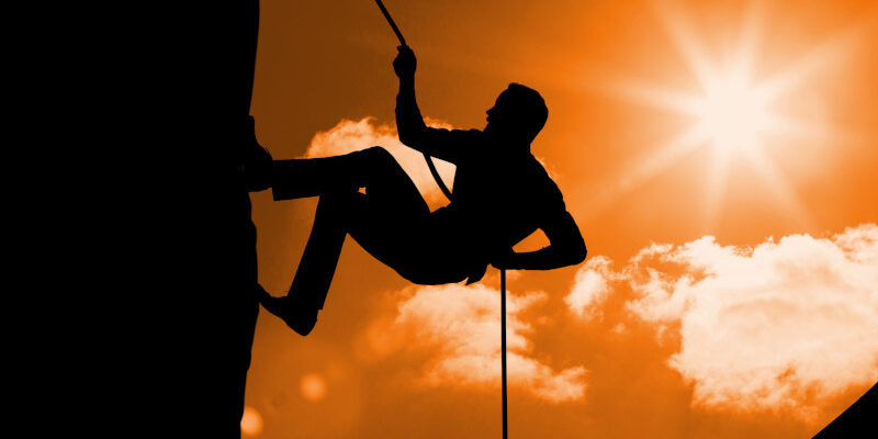 Silhouette of man climbing a mountain against sunny background