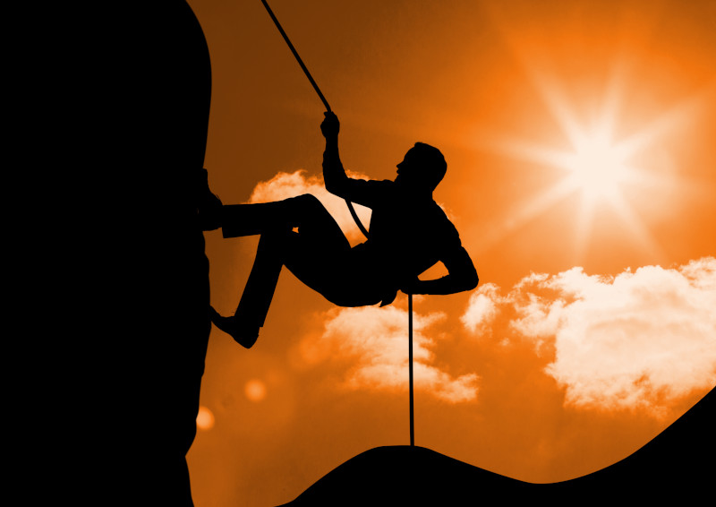 Silhouette of man climbing a mountain against sunny background
