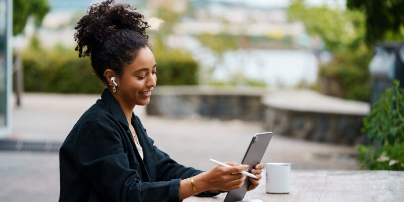 Woman using tablet whilst sitting outside drinking coffee