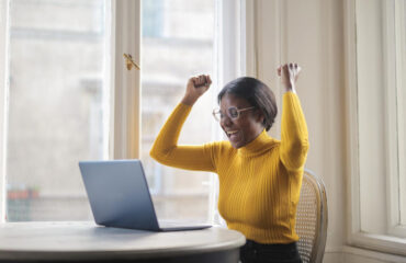 Woman siting in front of laptop with fists raised in celebration