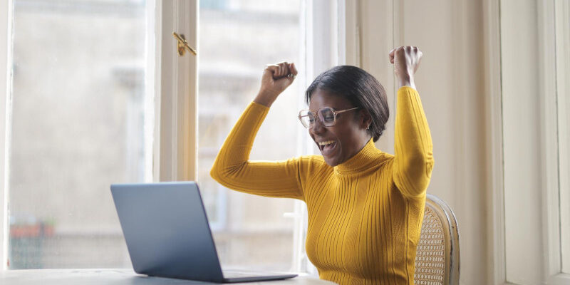 Woman siting in front of laptop with fists raised in celebration