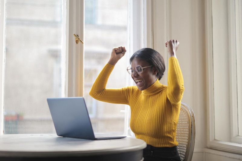 Woman siting in front of laptop with fists raised in celebration