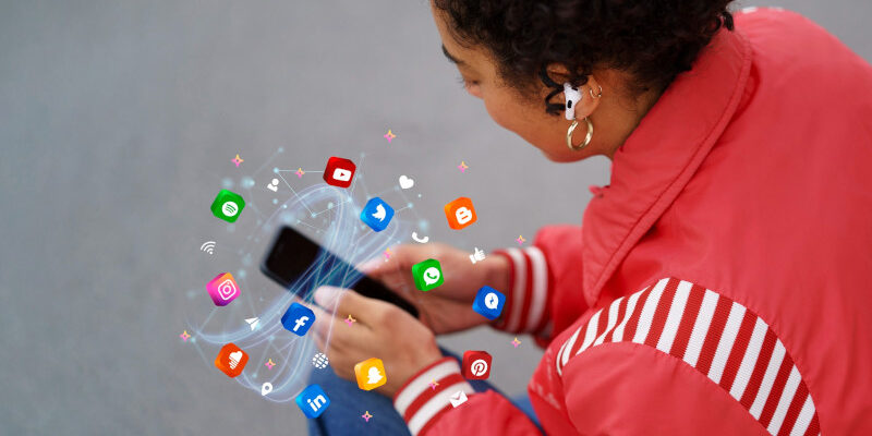 Woman holding smart phone with social media icons whirling around it