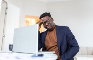 Stressed tired man touching temples using a laptop