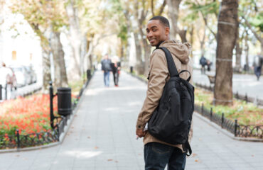 Young happy man wearing backpack walking on the street and looking back