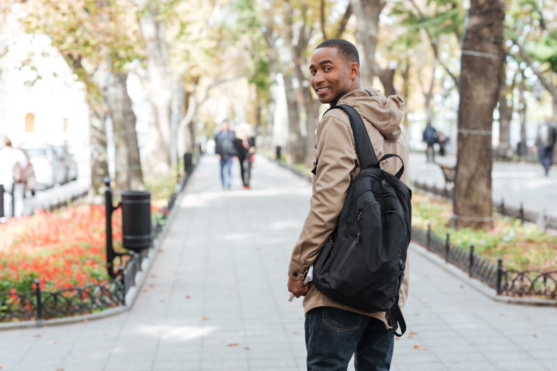 Young happy man wearing backpack walking on the street and looking back
