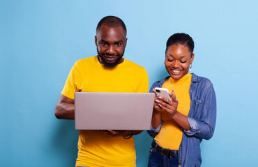 Happy man and woman using laptop computer and smartphone in studio