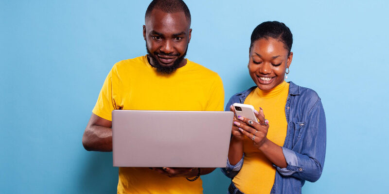 Happy man and woman using laptop computer and smartphone in studio