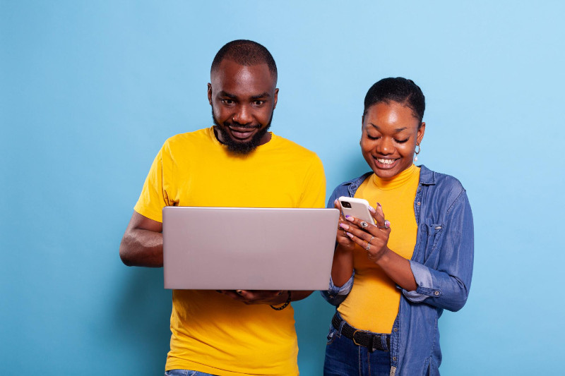 Happy man and woman using laptop computer and smartphone in studio