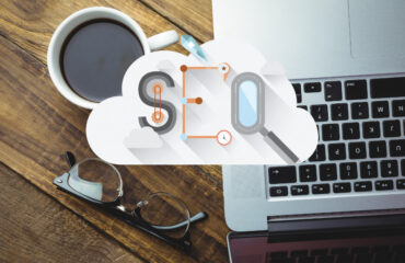 Top view of desk with laptop, pair of glasses and a cup of coffee with cloud having the word SEO in the foreground