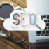 Top view of desk with laptop, pair of glasses and a cup of coffee with cloud having the word SEO in the foreground