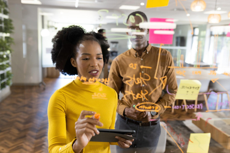 Man and woman in office brainstorming and writing on glass board