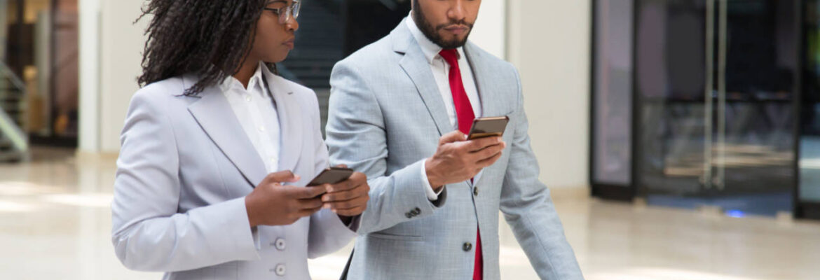 Business woman and business man conversing whilst walking and using mobile phones