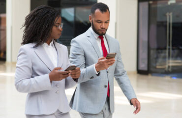 Business woman and business man conversing whilst walking and using mobile phones