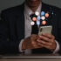 Concept of business man in a suit hlding a smartphone with a bubble of icons floating around it