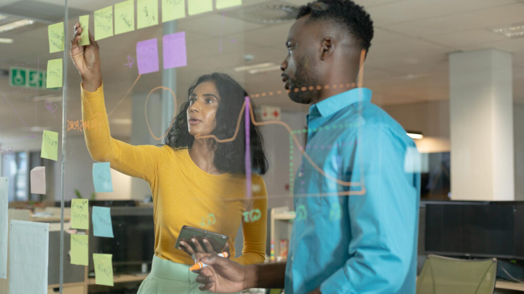 Young colleagues planning strategy over glass wall at modern workplace