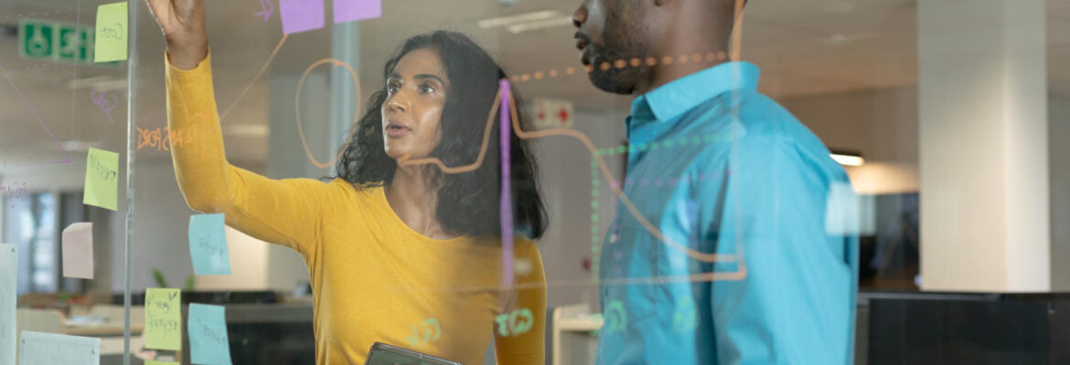 Young colleagues planning strategy over glass wall at modern workplace