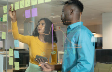 Young colleagues planning strategy over glass wall at modern workplace