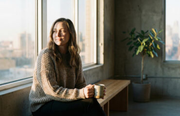 Woman Sitting on Bench at Sunrise Holding Coffee Mug